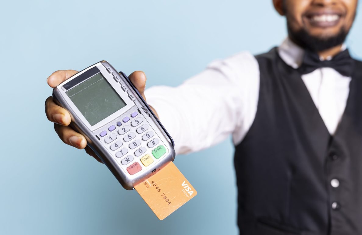 African american bellhop pointing at the pos terminal and asking for the payment, service oriented hospitality industry. Symbolizing electronic transaction for the lodging.